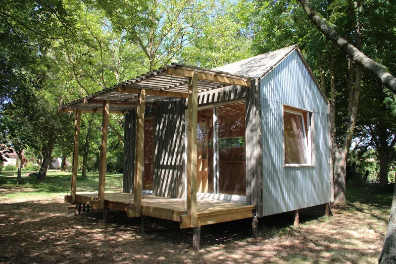 Angled view of the cabin showing corrugated metal walls and the timber pergola deck in dappled shade
