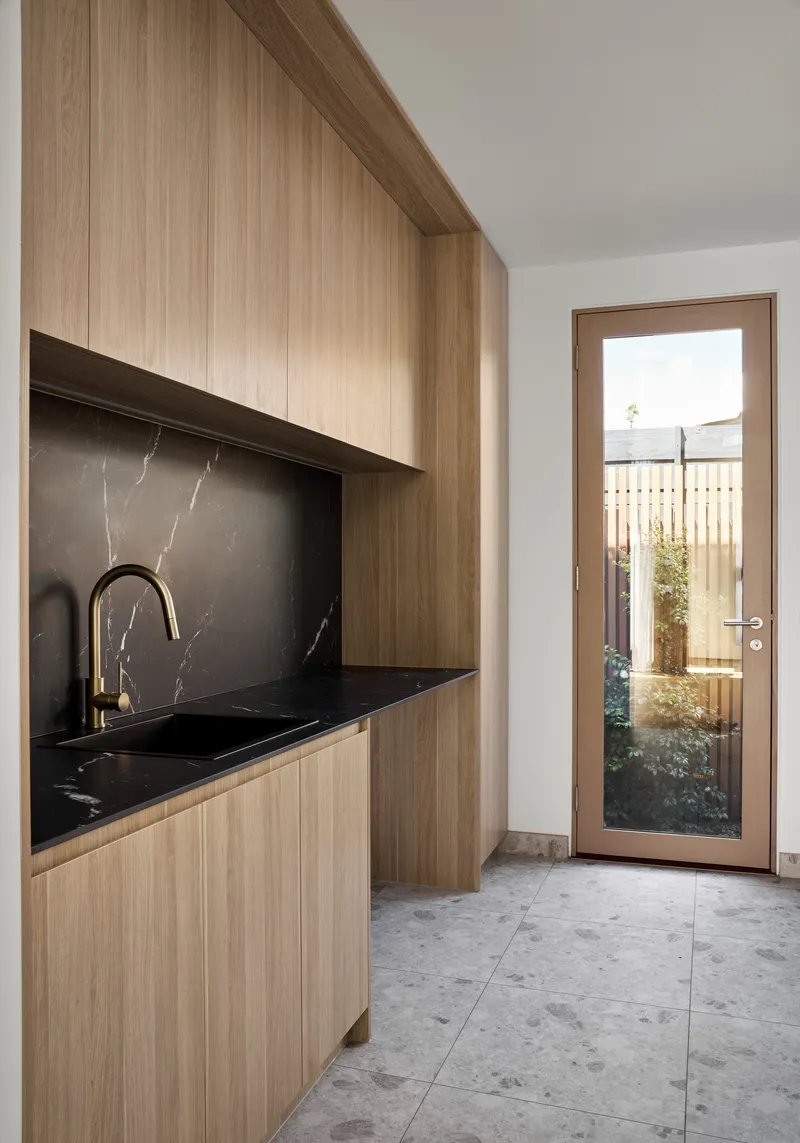 Timber cabinetry with black stone countertop and backsplash beside a glazed door to a planted courtyard