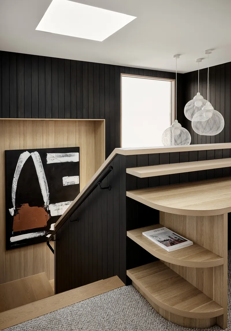 Curved timber stair treads against a black vertical panel wall with mesh pendant lights overhead