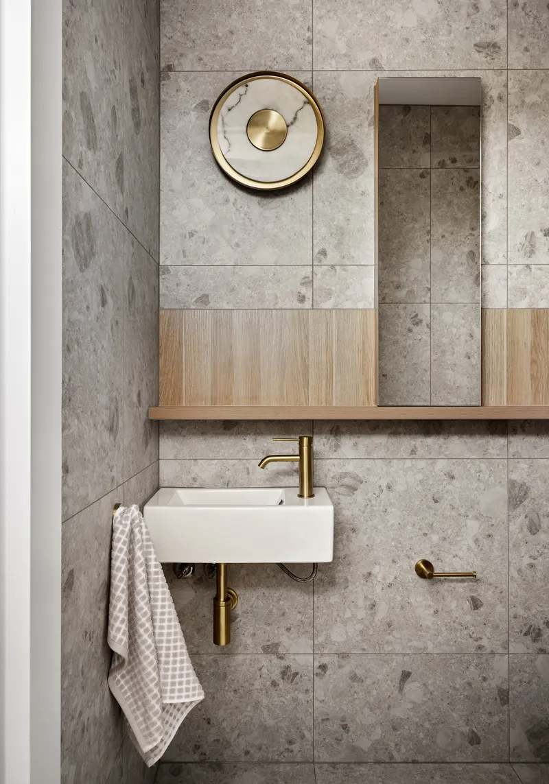 Wall-mounted basin with brass fittings below a timber and mirror cabinet on grey tile