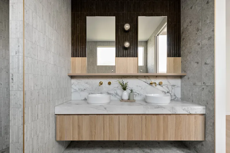 Double vanity with timber cabinetry and marble countertop beneath fluted black wall panel and twin mirrors
