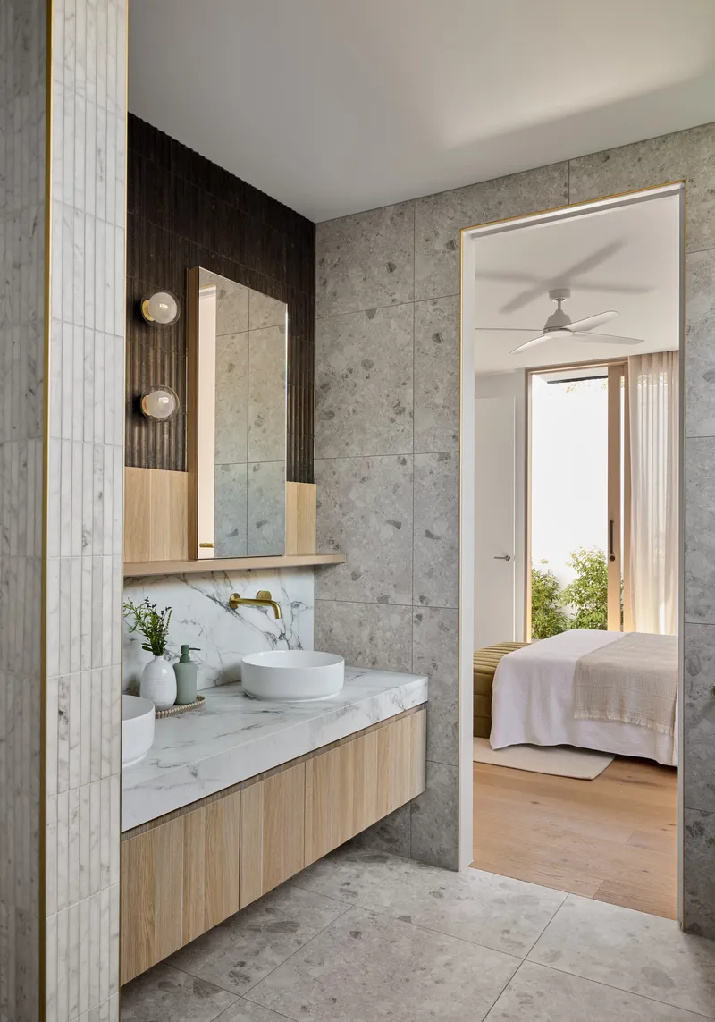 Bathroom vanity with view through doorway to bedroom with pale timber flooring and natural light