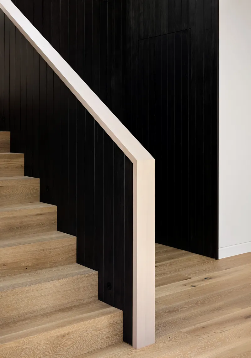 Timber stair with pale handrail ascending against black vertical timber cladding