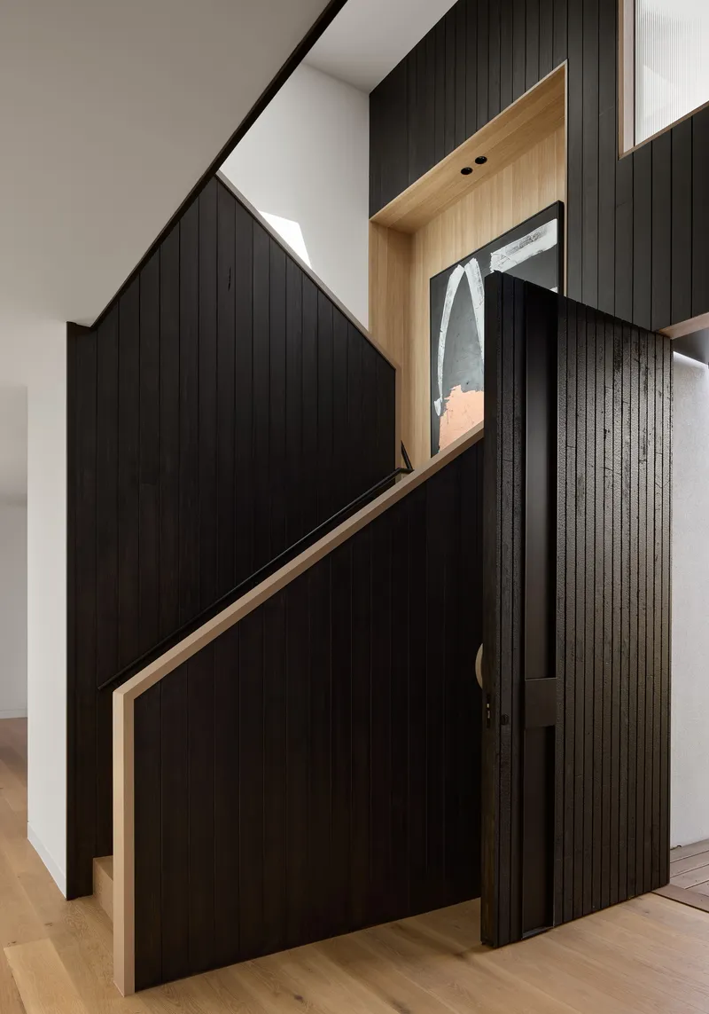 Understairs storage with black cladding and timber-lined display niche beneath angled stair soffit