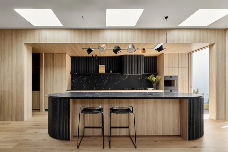Kitchen island with black marble countertop under three rectangular skylights and timber-clad walls and ceiling