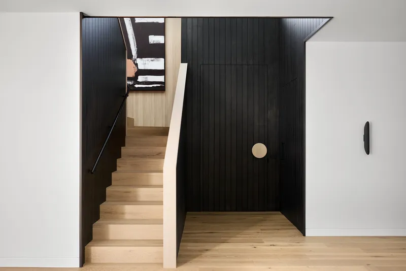Entry hall with black vertical paneling, light timber stairs, and a circular door pull detail