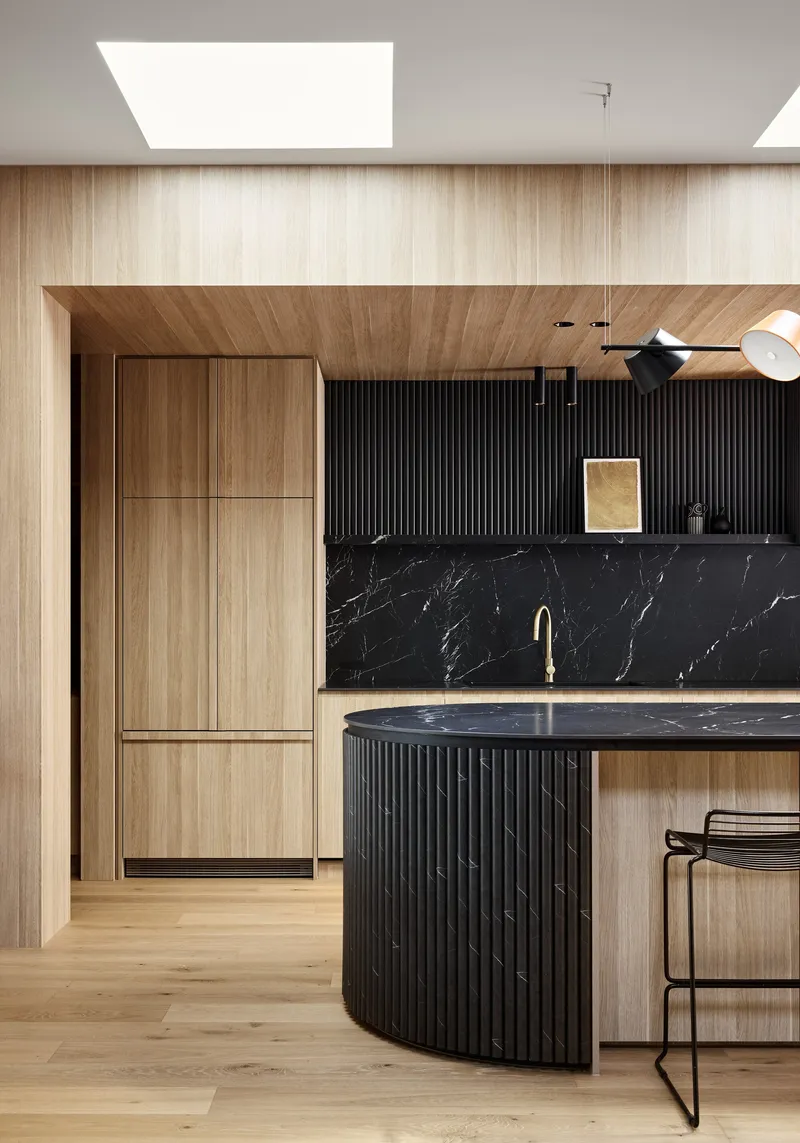 Kitchen with light timber cabinetry, black marble backsplash and fluted island under a rectangular skylight