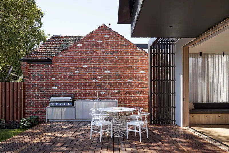Timber deck with outdoor dining beneath cantilever and against retained red brick gable wall