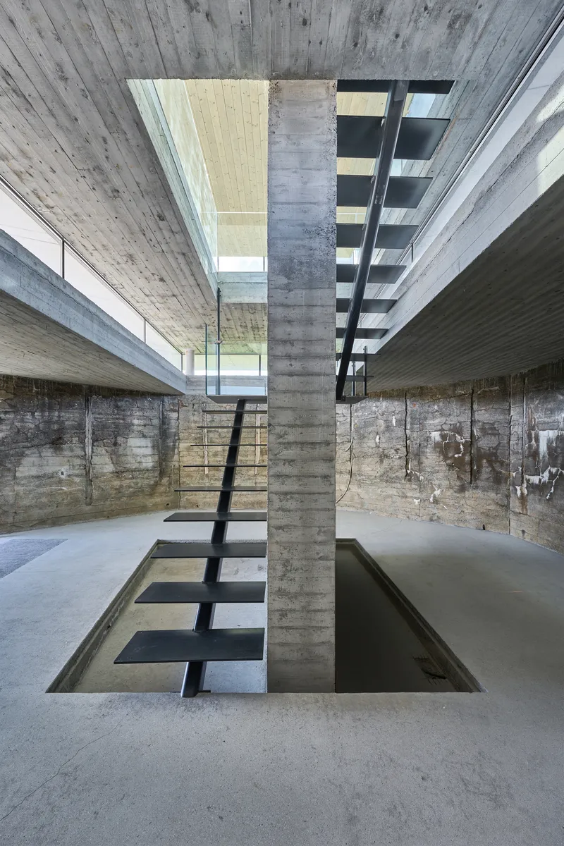 Steel stair spanning a water-filled void between board-formed concrete walls in the lower level