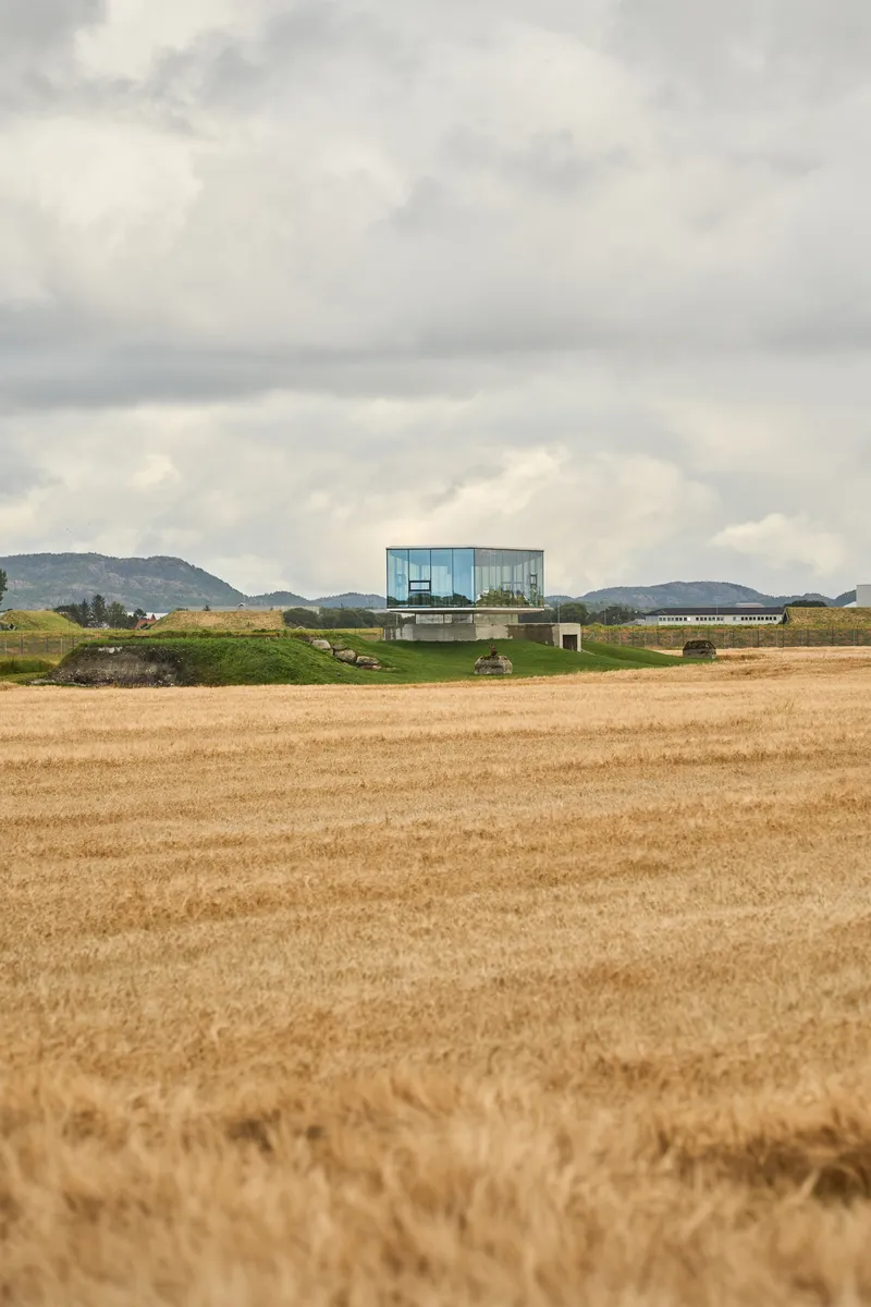 Distant view of the cantilevered structure in harvested fields beneath a heavy cloud cover and hills