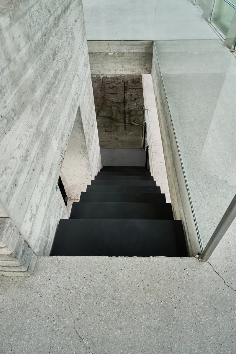 Top-down view of a steel staircase descending between board-formed concrete walls