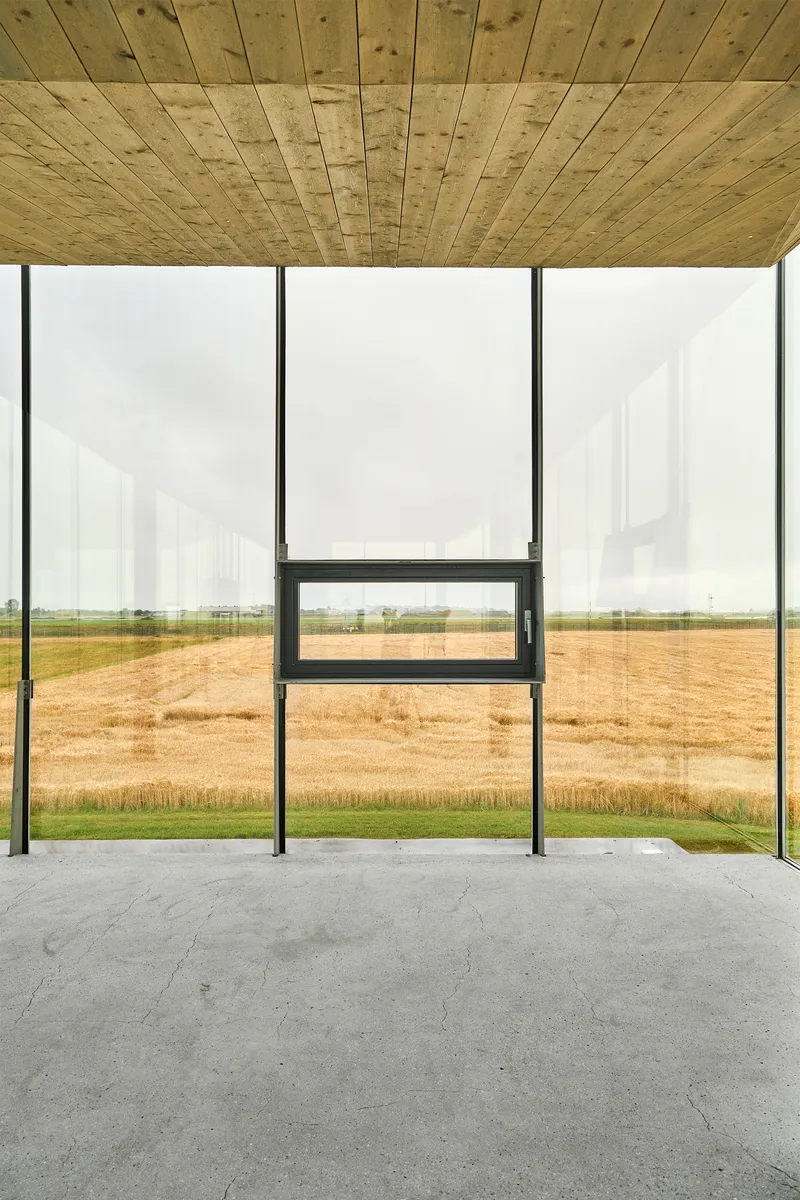 Timber plank ceiling above floor-to-ceiling glass walls framing harvested fields beyond