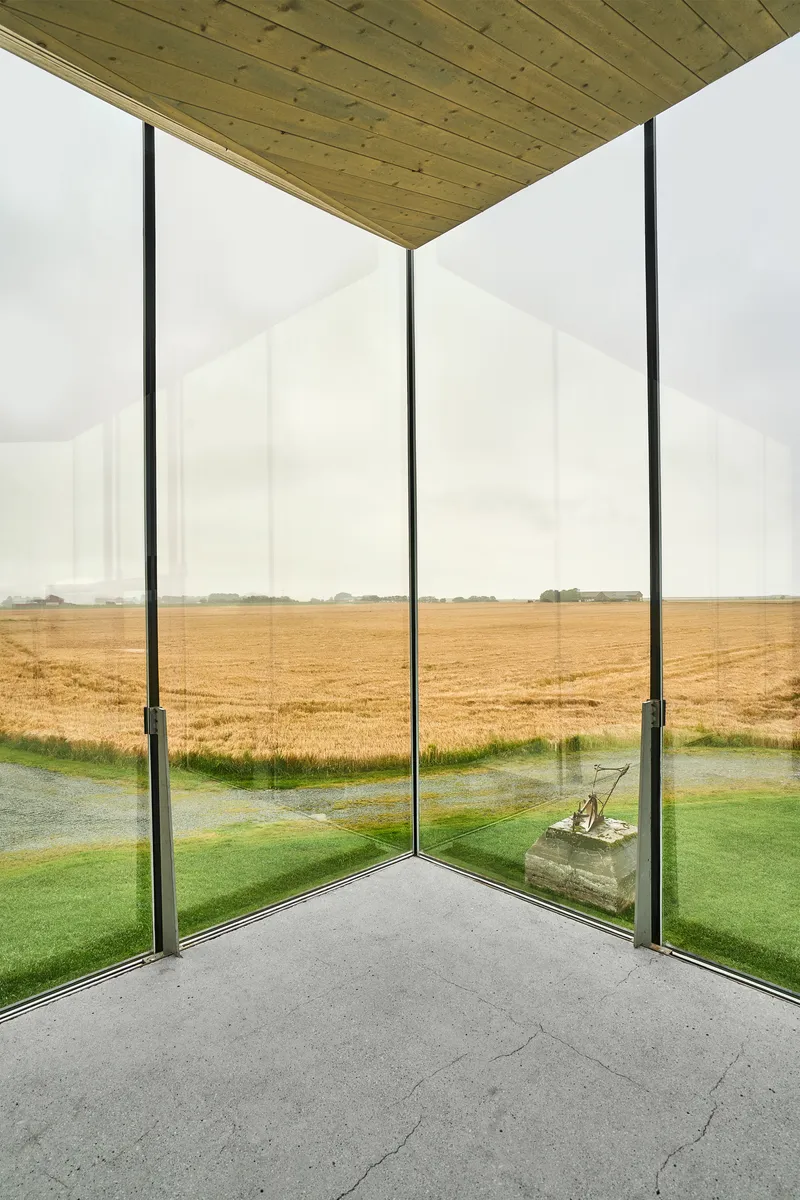 Corner glazing meeting at a steel column overlooking golden farmland and a reflecting pool