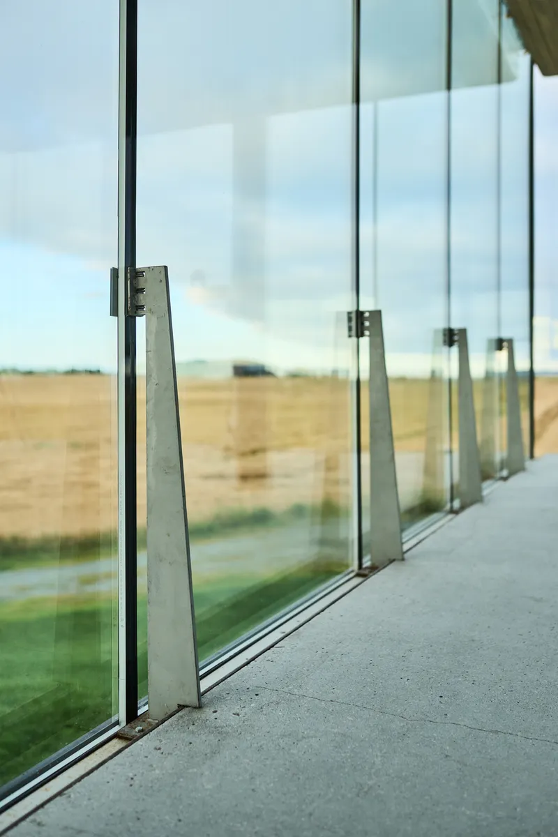 Close-up of angled steel brackets supporting the glass curtain wall and floor track
