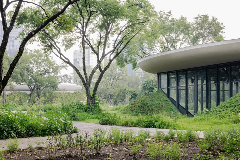 Curved glass facade embedded in a green-roofed berm beneath overhanging tree canopy