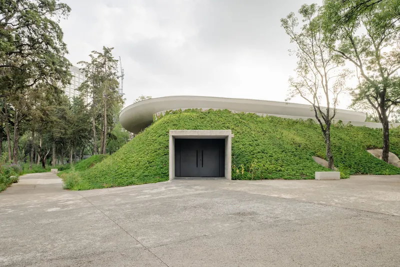 Entrance portal set into a planted earth berm beneath a curved cantilevered roof