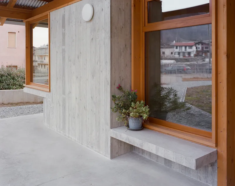 Concrete window seat with potted plant beneath timber-framed glazing overlooking a gravel courtyard