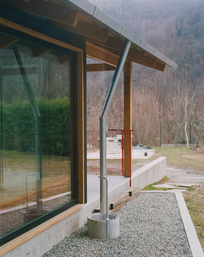 Exterior corner showing angled steel column supporting the timber roof overhang above a gravel terrace