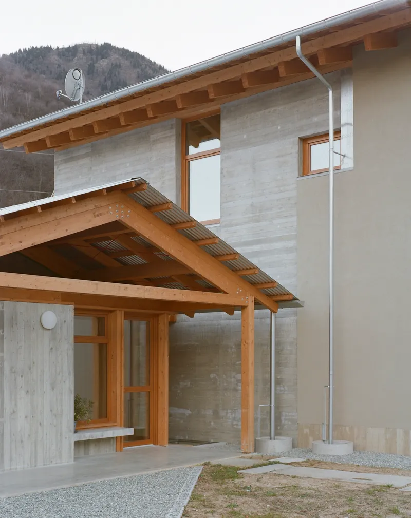 Entrance porch with exposed timber beams and concrete wall beside a wooded slope