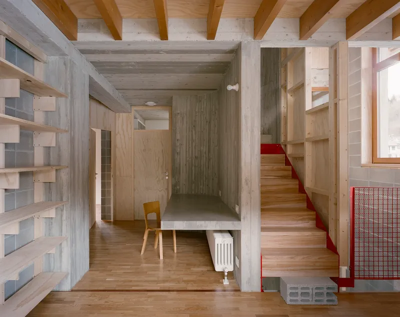 Entry hall with timber stair featuring red metal handrail and concrete structural frame