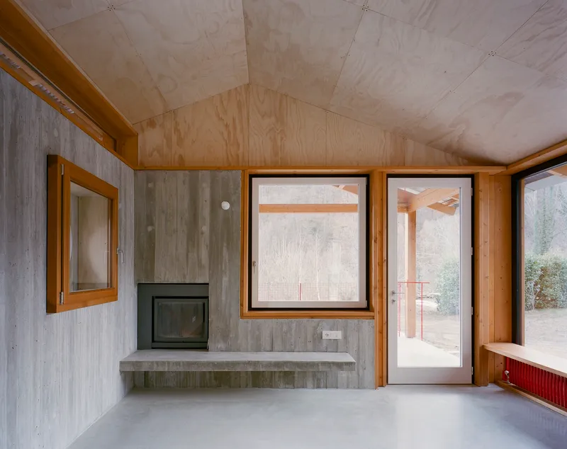 Interior room with plywood ceiling, board-formed concrete walls, and a corner fireplace