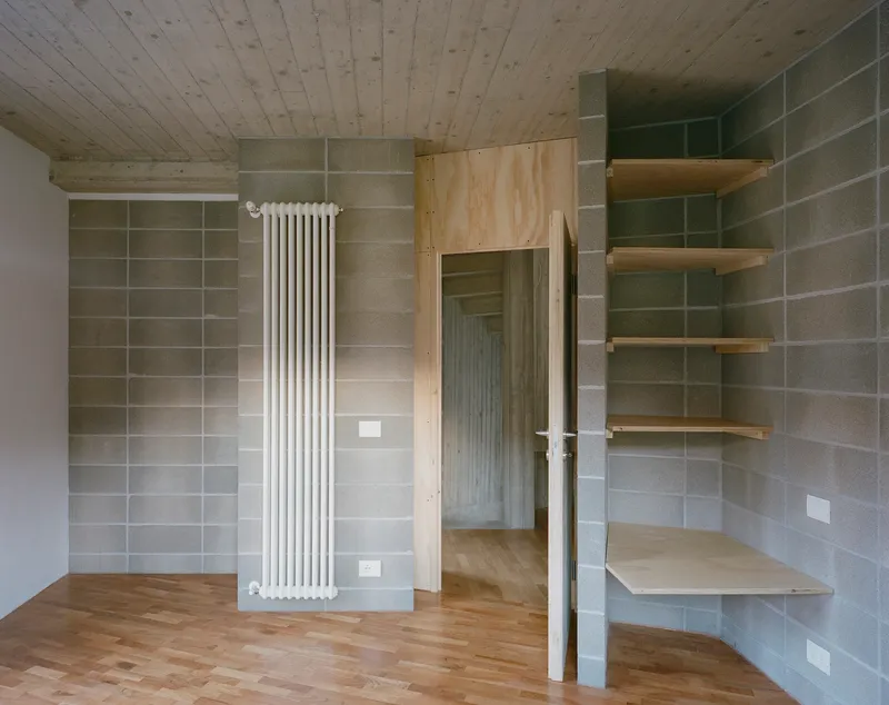 Corner view showing plywood door, radiator, and floating shelves against concrete block walls