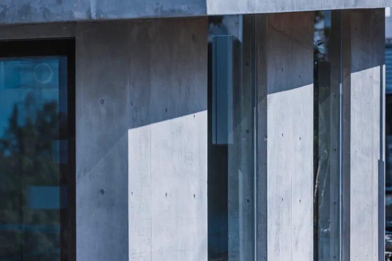 Close-up of concrete walls intersecting with steel-framed glass panels reflecting afternoon light