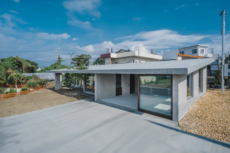 Single-story concrete pavilion with flat roof and glass walls overlooking a gravel courtyard
