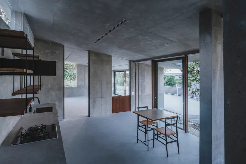 Open plan interior with concrete columns and ceiling, dining table near glazed doors opening to courtyard