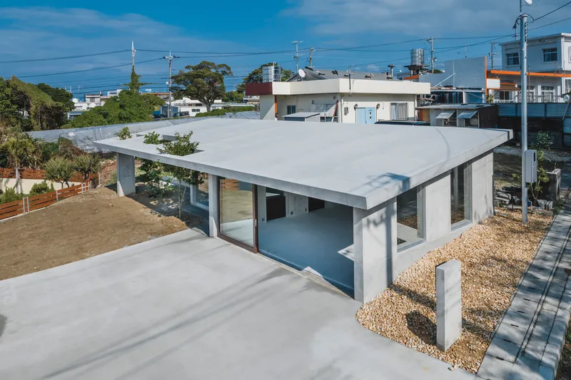 Corner view showing the elevated concrete roof plane supported by cylindrical columns over gravel ground