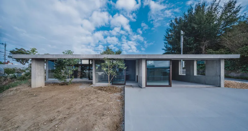 Front facade with concrete columns framing glazed openings and young planted trees under blue sky