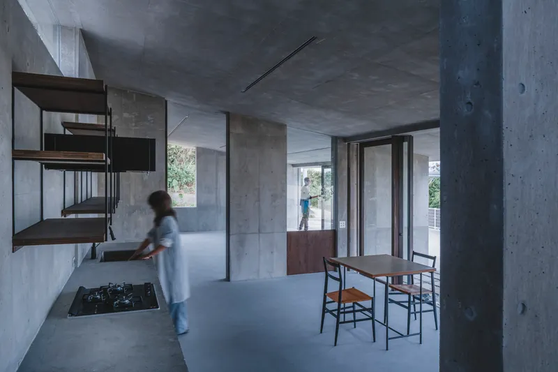 Interior kitchen and dining space with exposed concrete surfaces and a figure in motion