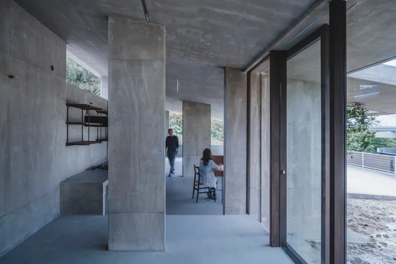 Two figures inhabit an open concrete interior with freestanding columns and a wall-mounted shelving unit
