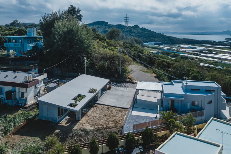 Aerial view of low-slung concrete volumes with flat roofs and planted courtyards among coastal residential development