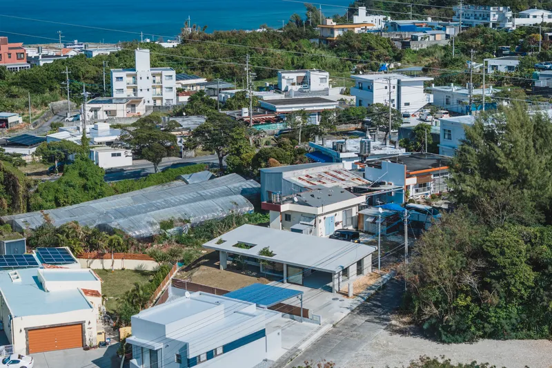 Aerial view of flat-roofed concrete volumes with planted courtyards nestled within a coastal neighborhood and greenery