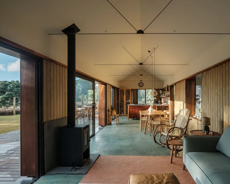 Open-plan living space with vertical timber cladding, plywood ceiling, and freestanding wood stove