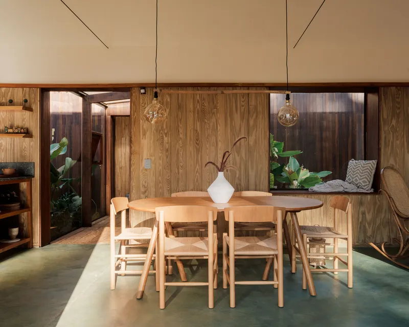 Dining table with timber chairs beneath pendant lights and timber-paneled walls with courtyard openings