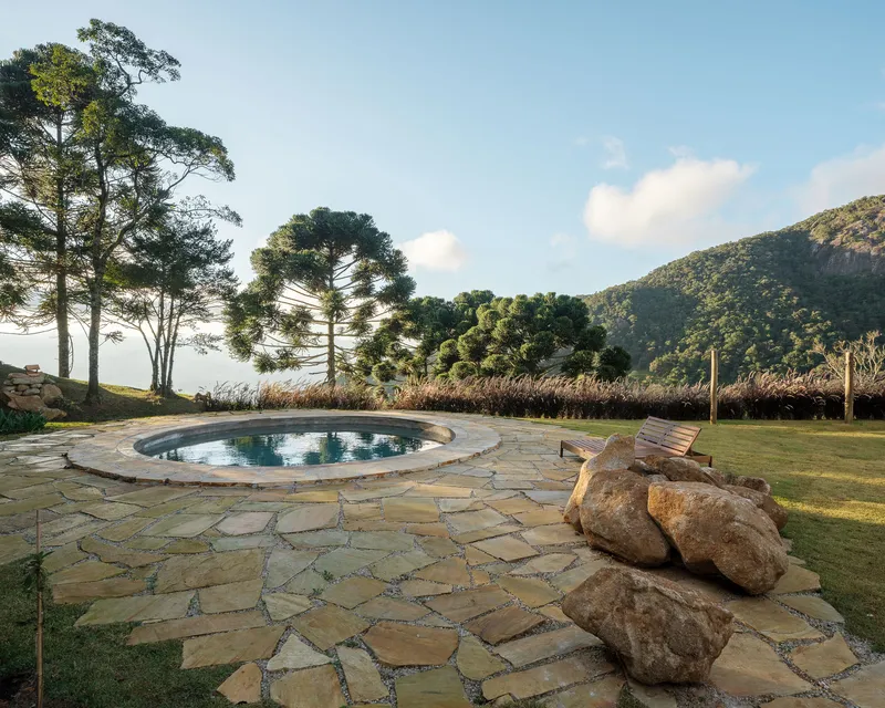 Circular pool surrounded by flagstone paving with boulders and grasses facing forested hills