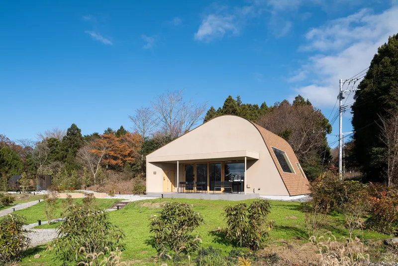 Curved pale roof structure with glazed openings set in a landscaped garden under clear blue sky