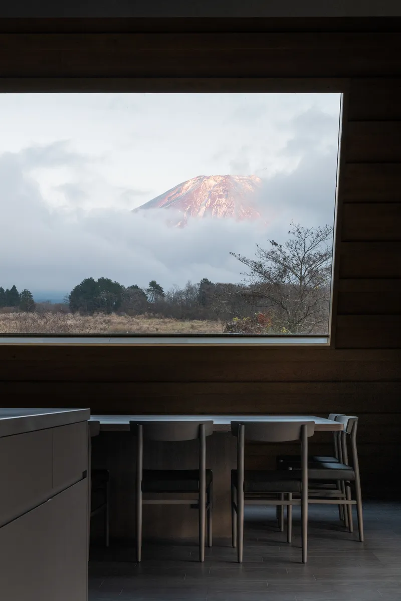 Horizontal window in timber-clad dining space framing a distant snowcapped mountain through clouds