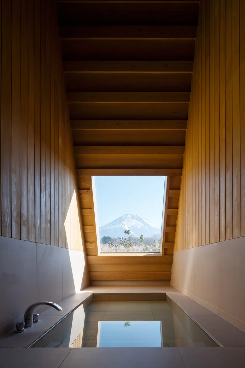 Sunken soaking tub with timber-lined ceiling and angled skylight framing a snowcapped volcano