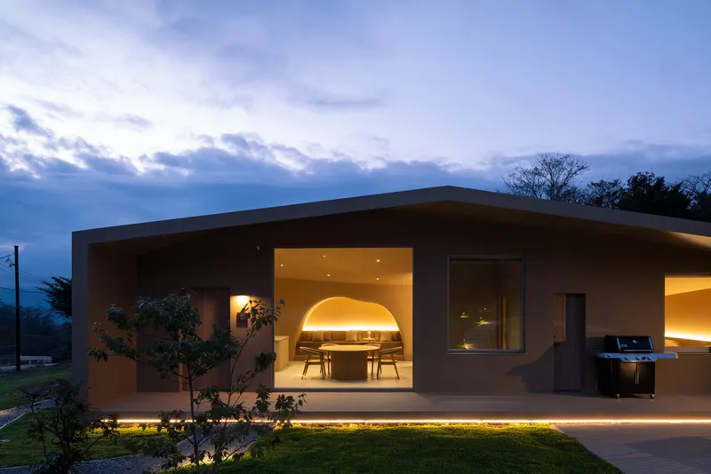 Curved roof overhang framing illuminated dining area with arched ceiling at dusk