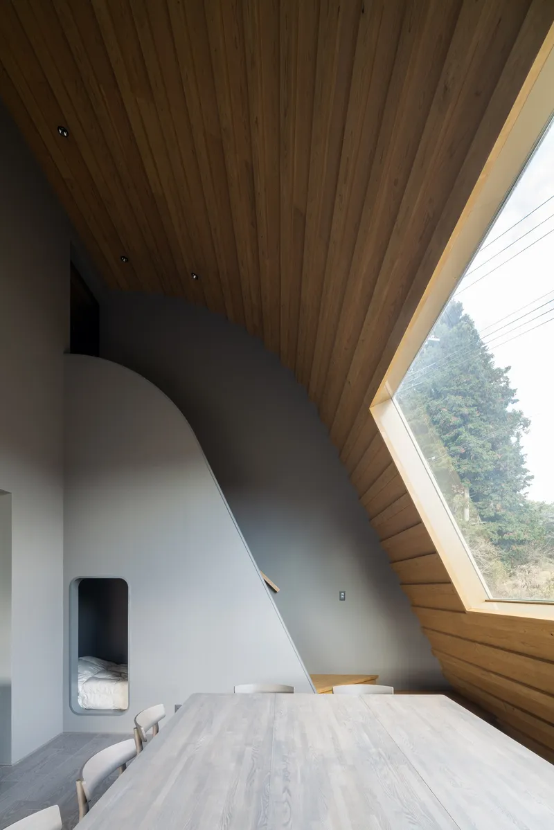 Bedroom with sloped timber ceiling and angled window revealing forest outside