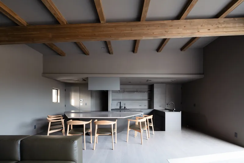 Open kitchen and dining area with exposed timber ceiling beams and grey walls in daylight
