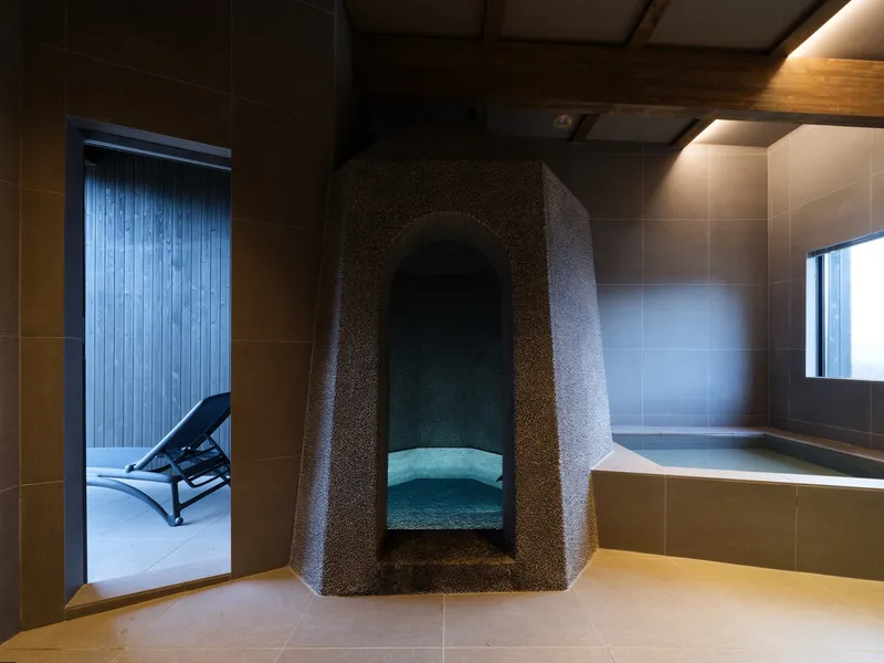 Textured stone alcove with integrated seating beside a soaking tub and timber-framed ceiling