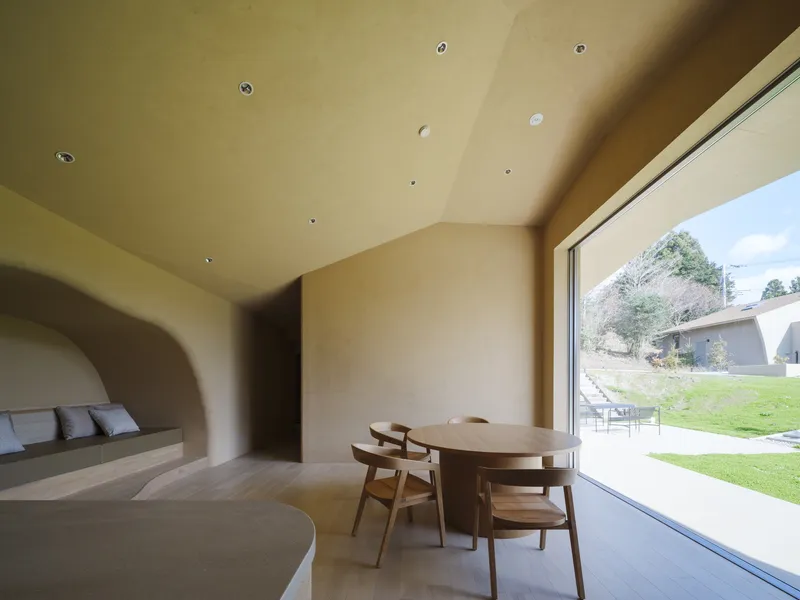 Open dining area with vaulted plywood ceiling and floor-to-ceiling window overlooking a green lawn