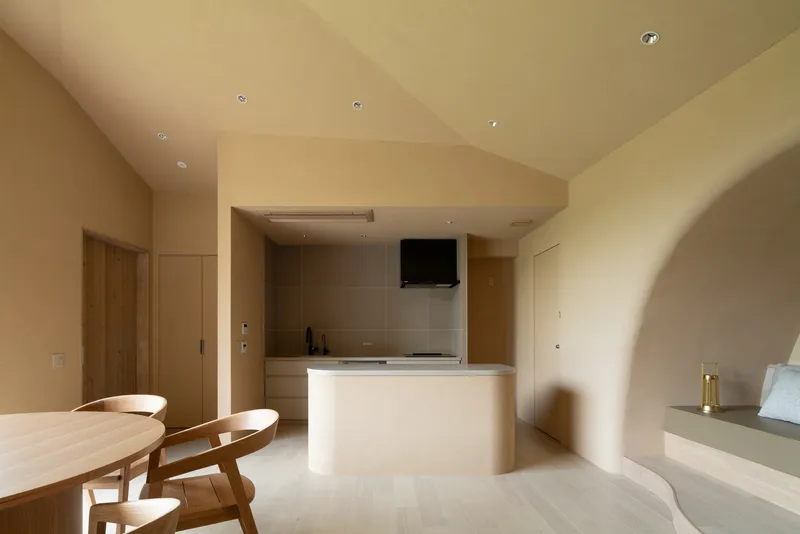 Interior view through arched opening toward the kitchen counter and dining table in pale timber