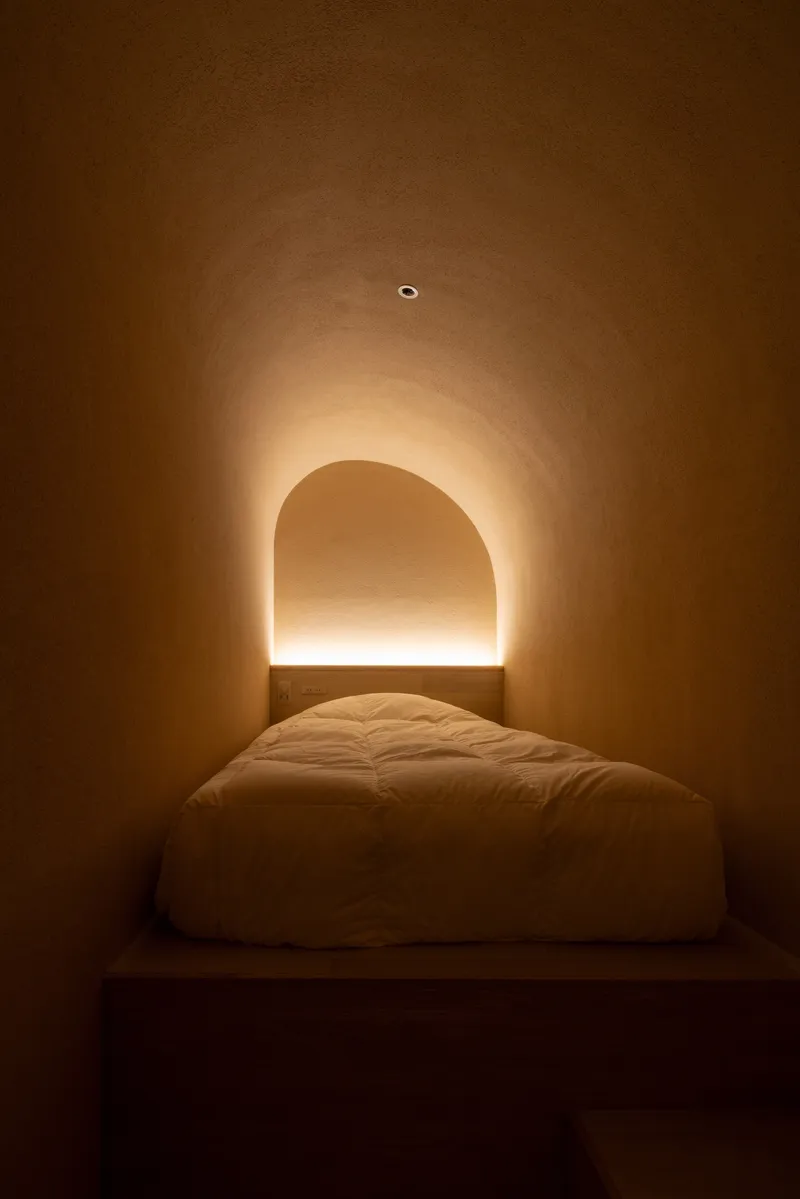 Bedroom alcove with arched niche and concealed linear lighting glowing above the platform bed at night