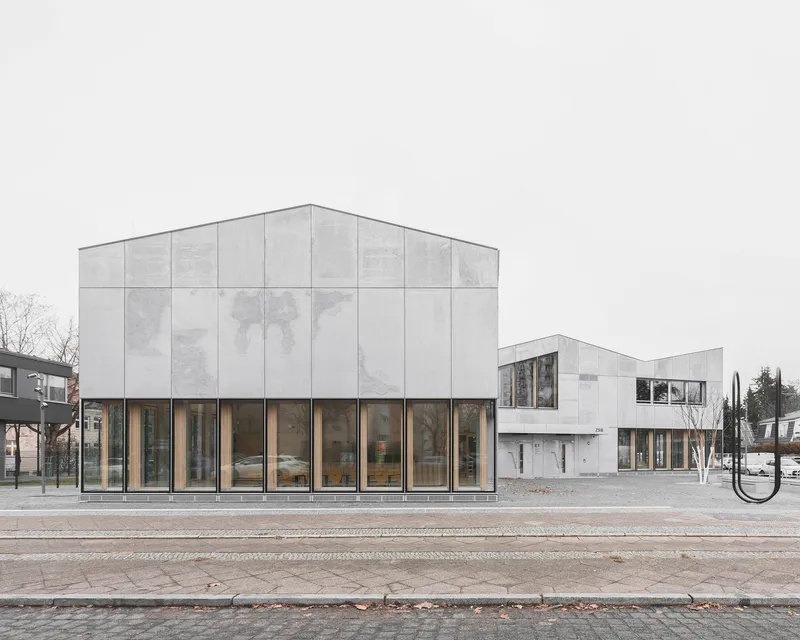 Street view of paneled concrete facade volumes with tall glazed ground floor openings on a grey day