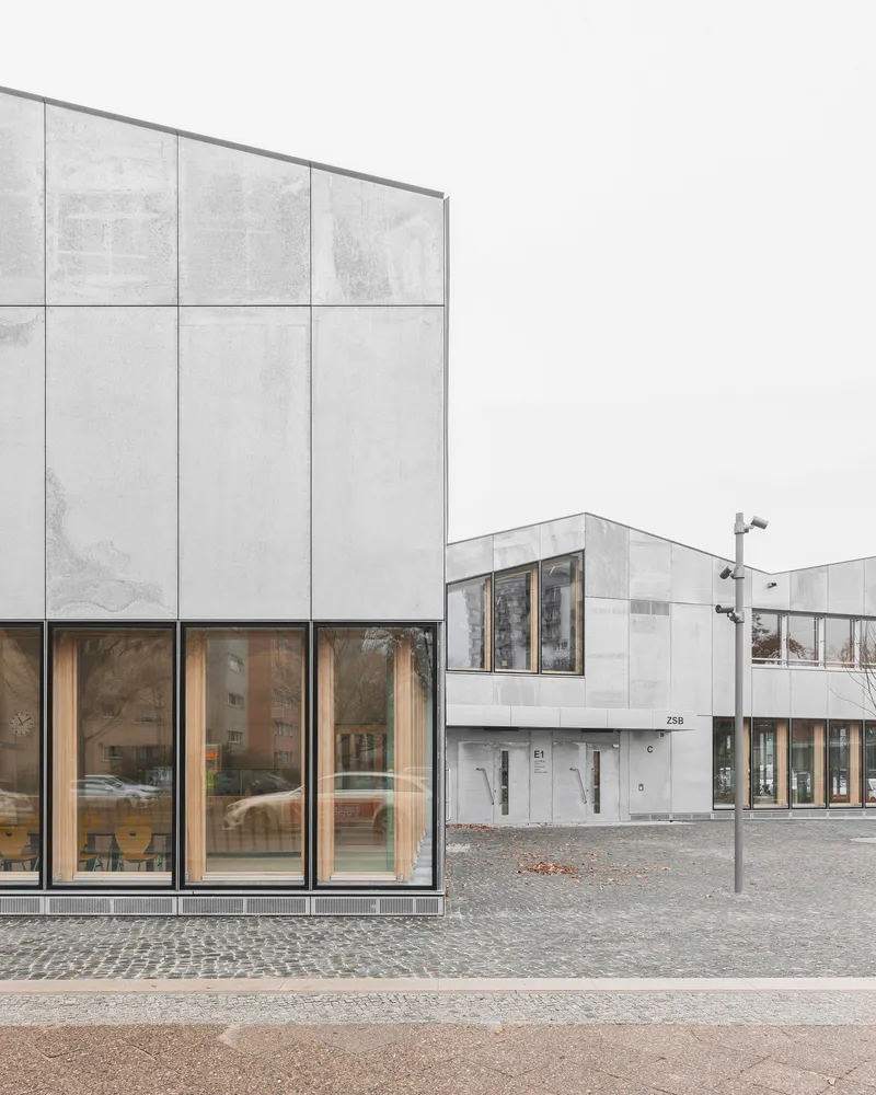 Close view of concrete panel facade with timber framed glazing reflecting neighboring buildings and street lamp